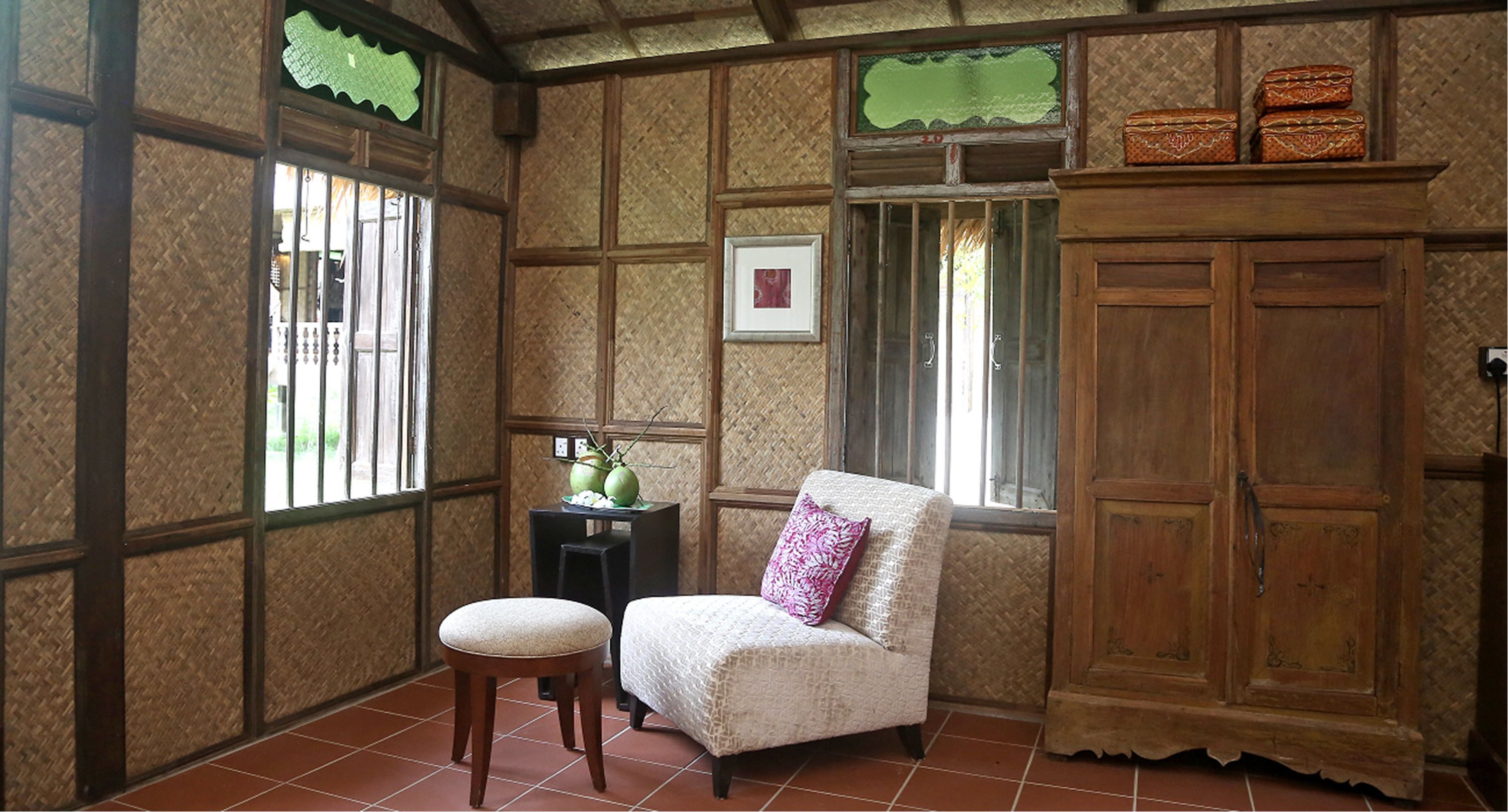 A room with a wooden cabinet, a chair with a cushion, a small table with a decorative item, and a window with bars.