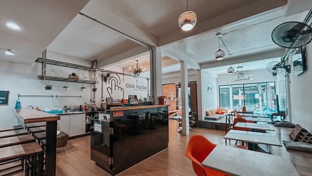 A modern hostel interior with a central bar, seating areas, and a visible sign reading "click Hostel". - Click Hostel (Bangkok)