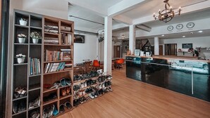 A spacious reception area with a wooden floor, a reception desk, and a chandelier. There are bookshelves and a shoe rack with various items. - Click Hostel (Bangkok)