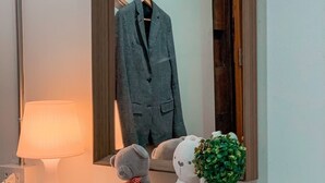A mirror with a wooden frame, a grey suit, a teddy bear, slippers, and a small potted plant on a white dresser. - Click Hostel (Bangkok)