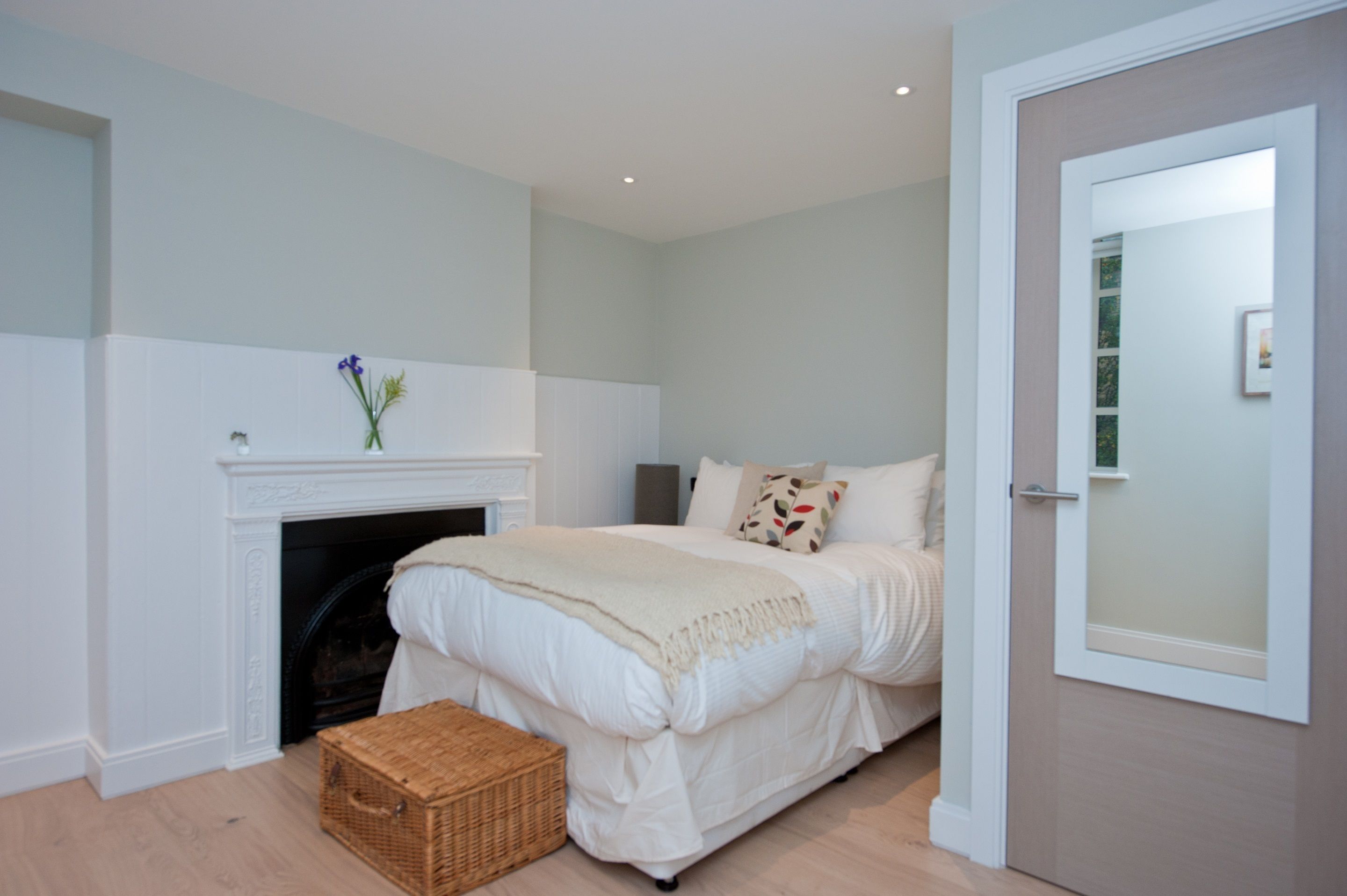 A bedroom with a fireplace, a bed with white bedding, a wicker basket, and a door with frosted glass.