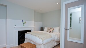 A bedroom with a fireplace, a bed with white bedding, a wicker basket, and a door with frosted glass. - The London Agent Spitalfields (London)