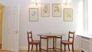 A dining area with a round wooden table and two chairs, flanked by framed botanical prints on the wall. - The London Agent Hyde Park King Bed (London)