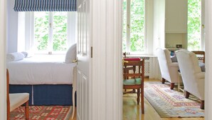 A bedroom with a bed, a chair, a desk, and a window with a view of greenery. - The London Agent Hyde Park King Bed (London)