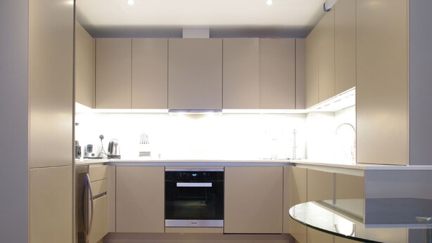 A modern kitchen with built-in appliances, a glass dining table, and wooden flooring. - The London Agent Waterloo Comfortable Home (London)