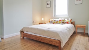 A bedroom with a wooden bed, a bedside table, a nightstand, a window, and a wall-mounted picture. - The London Agent Waterloo Comfortable Home (London)