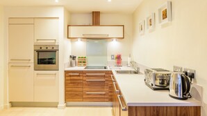 A modern kitchen with a built-in oven, a stainless steel range, wooden cabinets, a sink, a toaster, and a kettle.