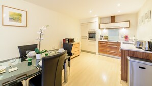 A modern kitchen with stainless steel appliances, wooden cabinets, and a dining area with a glass table and chairs.