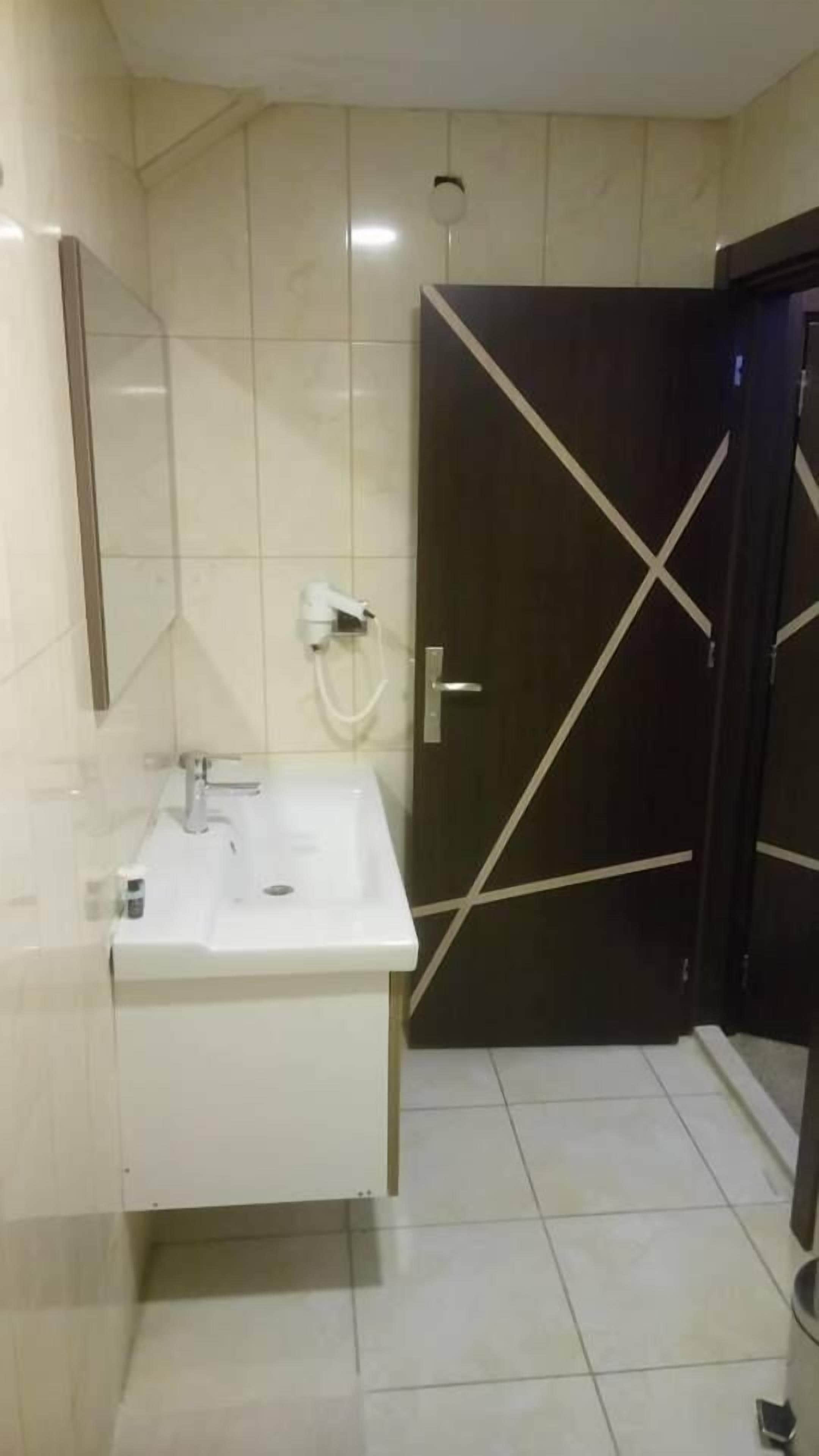 Un baño con un lavamanos blanco, un espejo y una puerta oscura con un diseño en forma de X blanca.