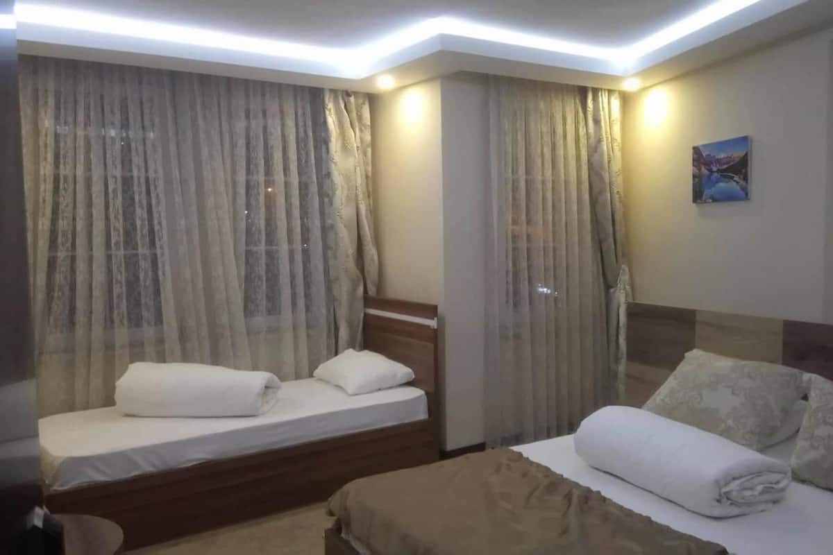 A hotel room with two beds, a headboard, a painting on the wall, and a window with curtains.