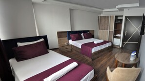 Una camera d'albergo con due letti, pavimento in legno, un tavolino rotondo con una sedia e un armadio con specchio.