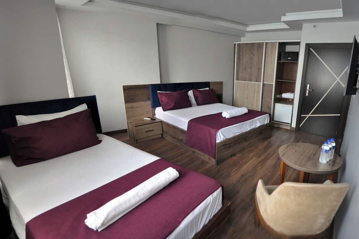 A hotel room with two beds, a wooden floor, a small round table with a chair, and a wardrobe with a mirror.