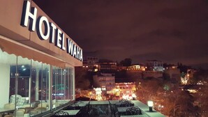 Un hotel chiamato "HOTEL WAHA" con posti a sedere all'aperto e vista sulla città di notte.
