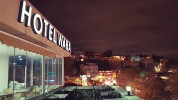 Un hotel llamado "HOTEL WAHA" con terraza exterior y vistas a la ciudad de noche.