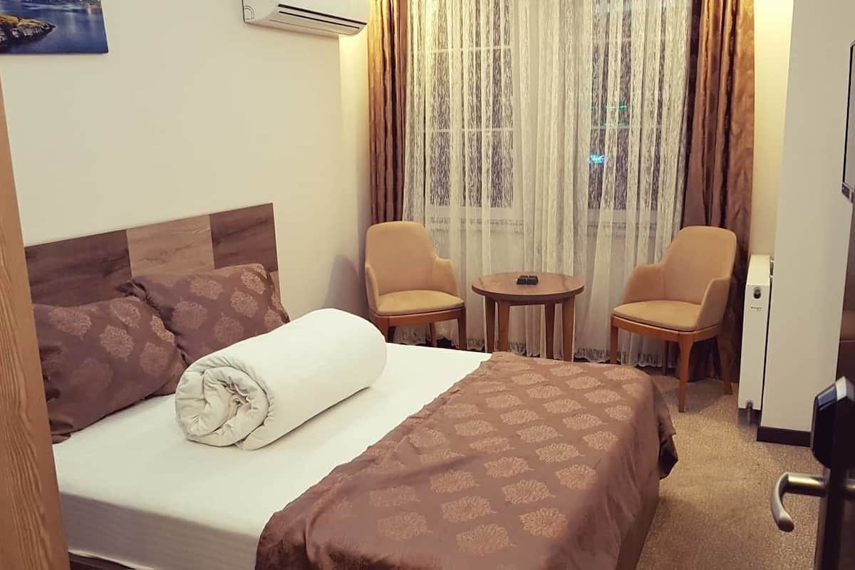 A hotel room with a bed, two chairs, a small table, and a door.