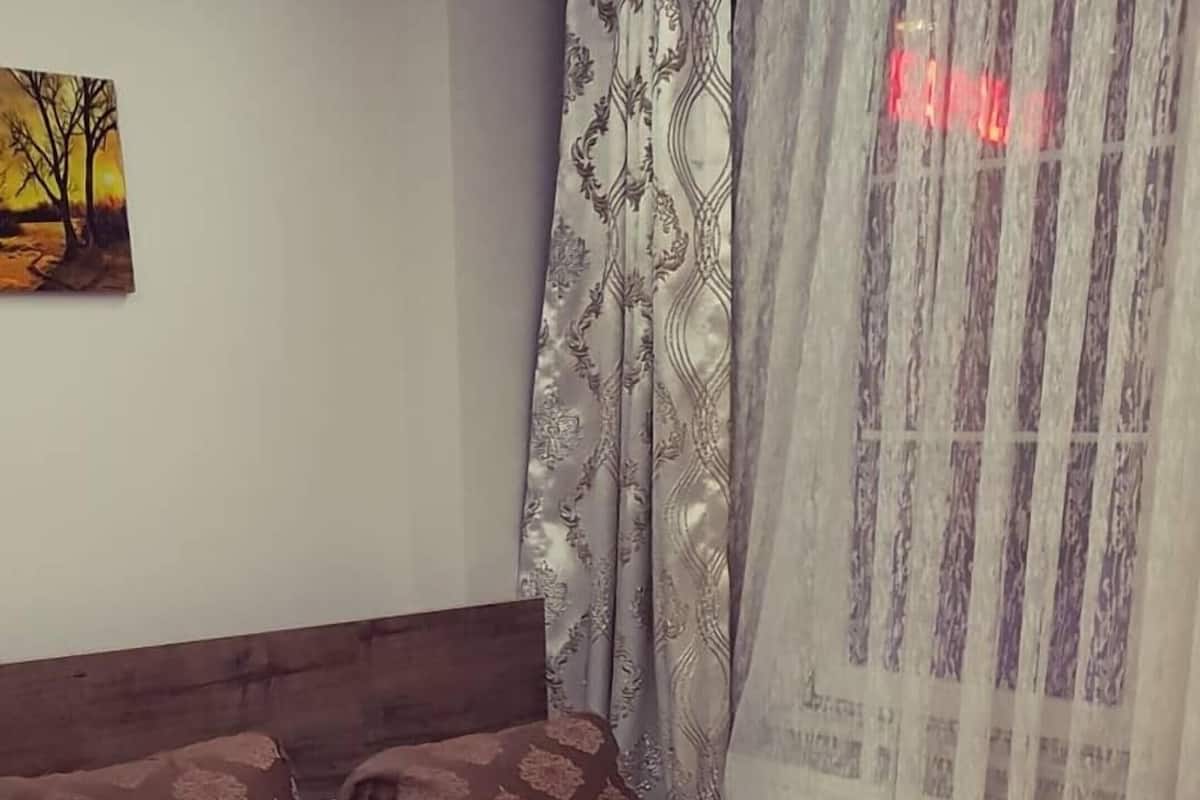 A neatly made bed with a brown patterned bedspread, a rolled white towel, and a brown pillow.