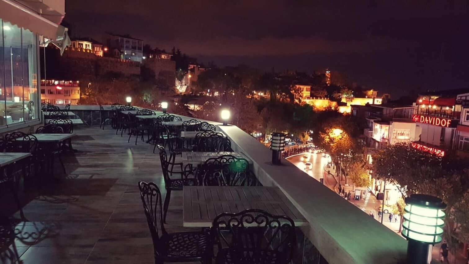 Terraza en la azotea con mesas y sillas, con vistas a un paisaje urbano nocturno.