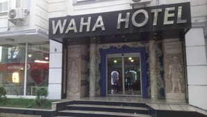 Esterno dell'Hotel Waha, con un grande cartello, ingresso in vetro e dettagli architettonici classici.