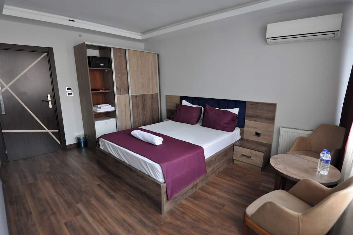 A hotel room with a bed, a wardrobe, a chair, and an air conditioning unit.