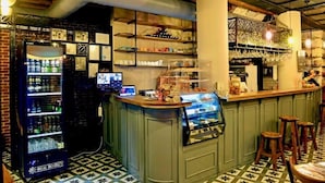 A bar area with a counter, stools, a beverage dispenser, and shelves with glasses and bottles. - Lotus Apart Pansiyon (Koycegiz)