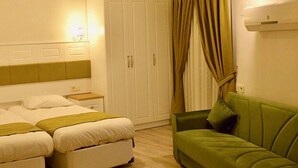 A hotel room with two beds, a green sofa, a wardrobe, and a wall-mounted air conditioner. - Lotus Apart Pansiyon (Koycegiz)