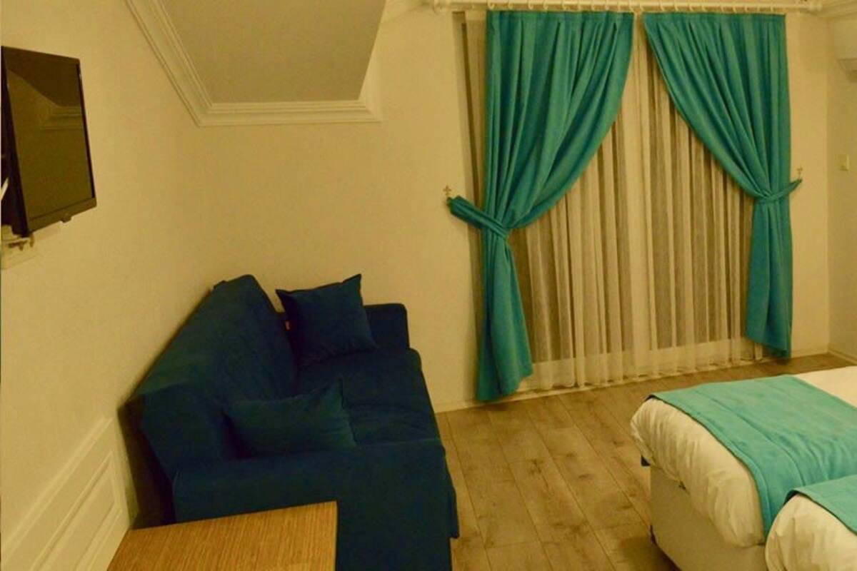 A hotel room with a bed, a chair, a nightstand, and a window with curtains.