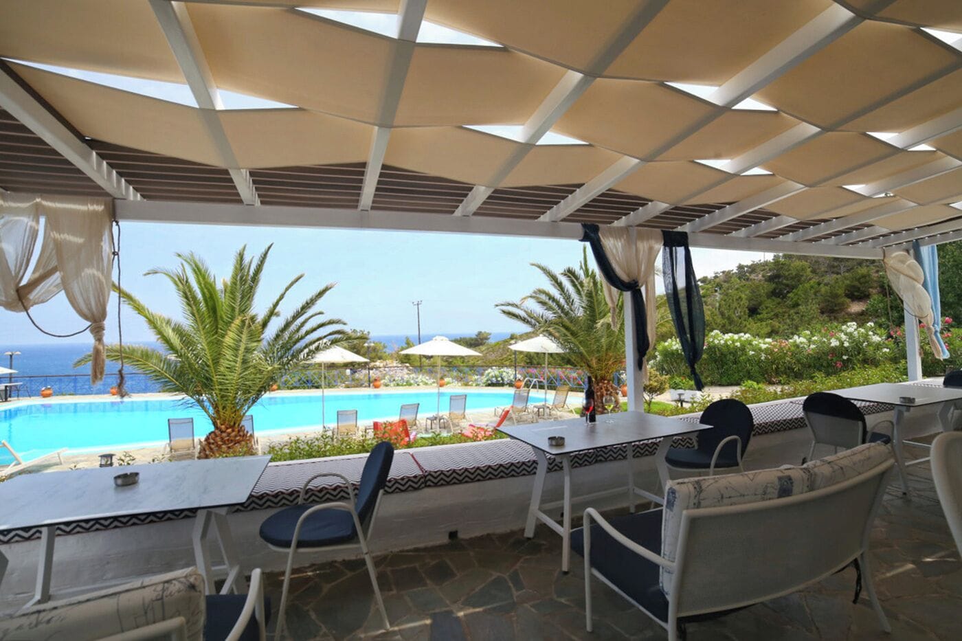 Un espace extérieur aménagé avec des sièges, donnant sur la piscine, abrité par une pergola et comprenant des chaises et des tables.