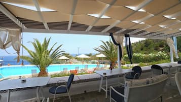 Un espace extérieur aménagé avec des sièges, donnant sur la piscine, abrité par une pergola et comprenant des chaises et des tables.