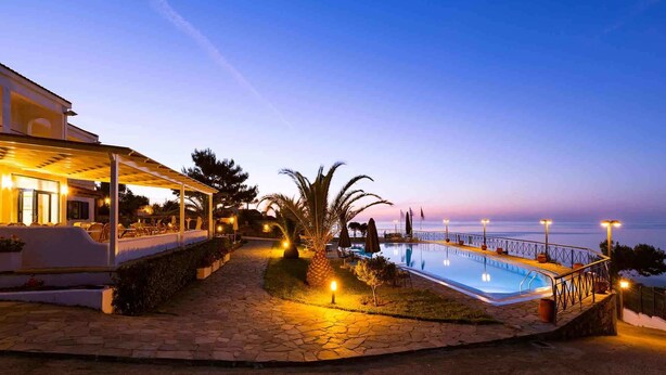 Área da piscina com espaço de estar coberto e vista para o mar ao entardecer.