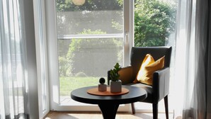 A room with a large window, a round table with a plant, and a chair with a cushion. - Hotel Blauer Fasan (Wiesmoor)
