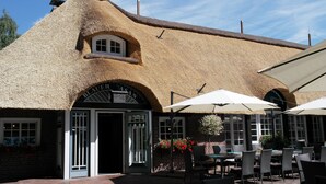 A thatched-roof building with a brick facade, outdoor seating area with umbrellas, and a sign reading "Bierhaus." - Hotel Blauer Fasan (Wiesmoor)