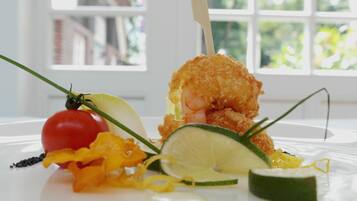 A seafood dish with a shrimp on a stick, garnished with lemon and herbs, on a white plate.