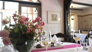 A dining table with a vase of flowers, wine glasses, and a pink tablecloth. - Hotel Blauer Fasan (Wiesmoor)