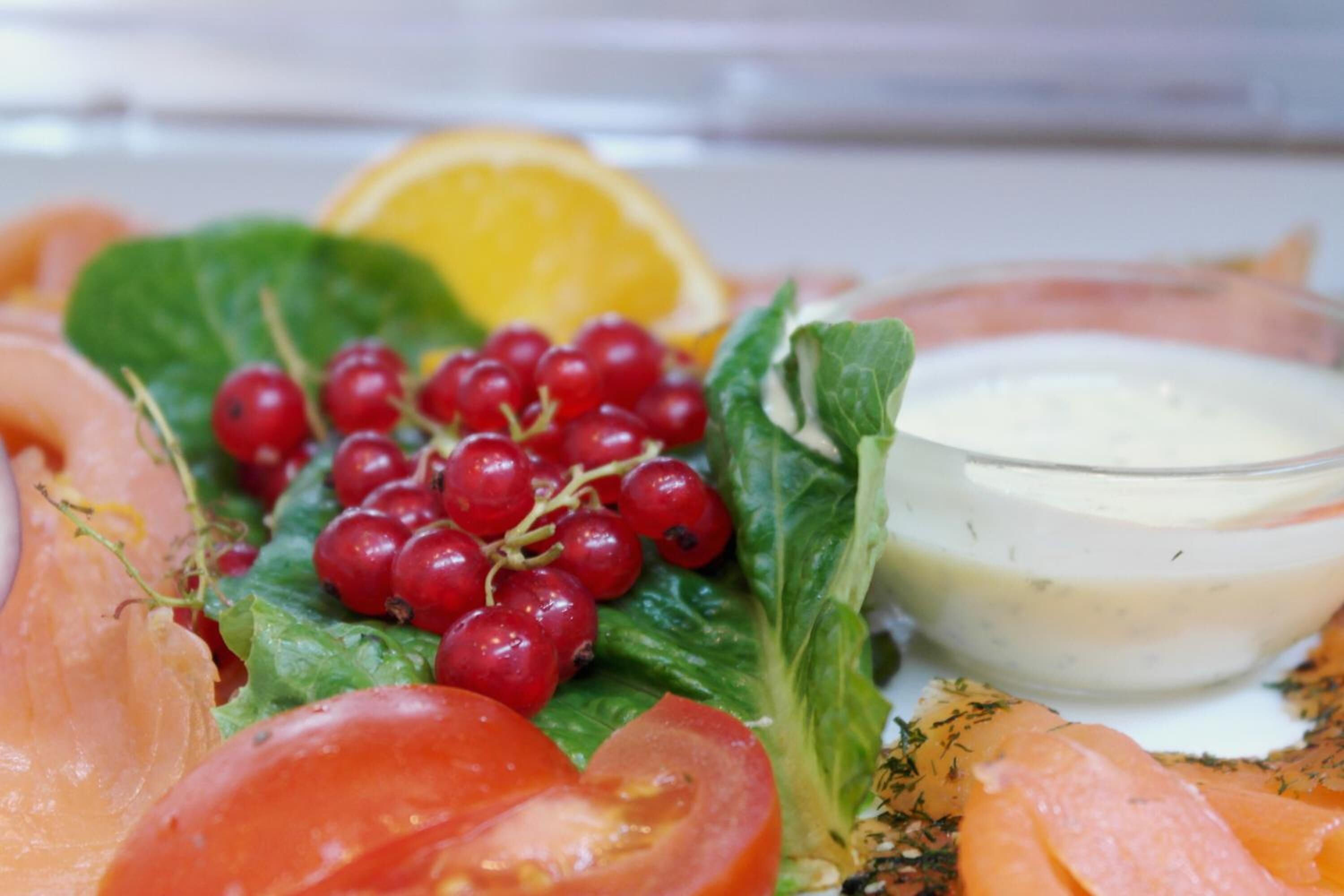 Un plato de salmón ahumado, verduras frescas, tomates cherry y un recipiente pequeño con salsa.