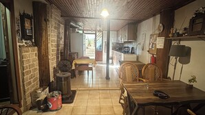 A cozy, rustic interior with a wooden ceiling, a dining area with a table and chairs, a kitchen in the background, and a fireplace with a stone wall. - Kont Pansiyon (Antalya)