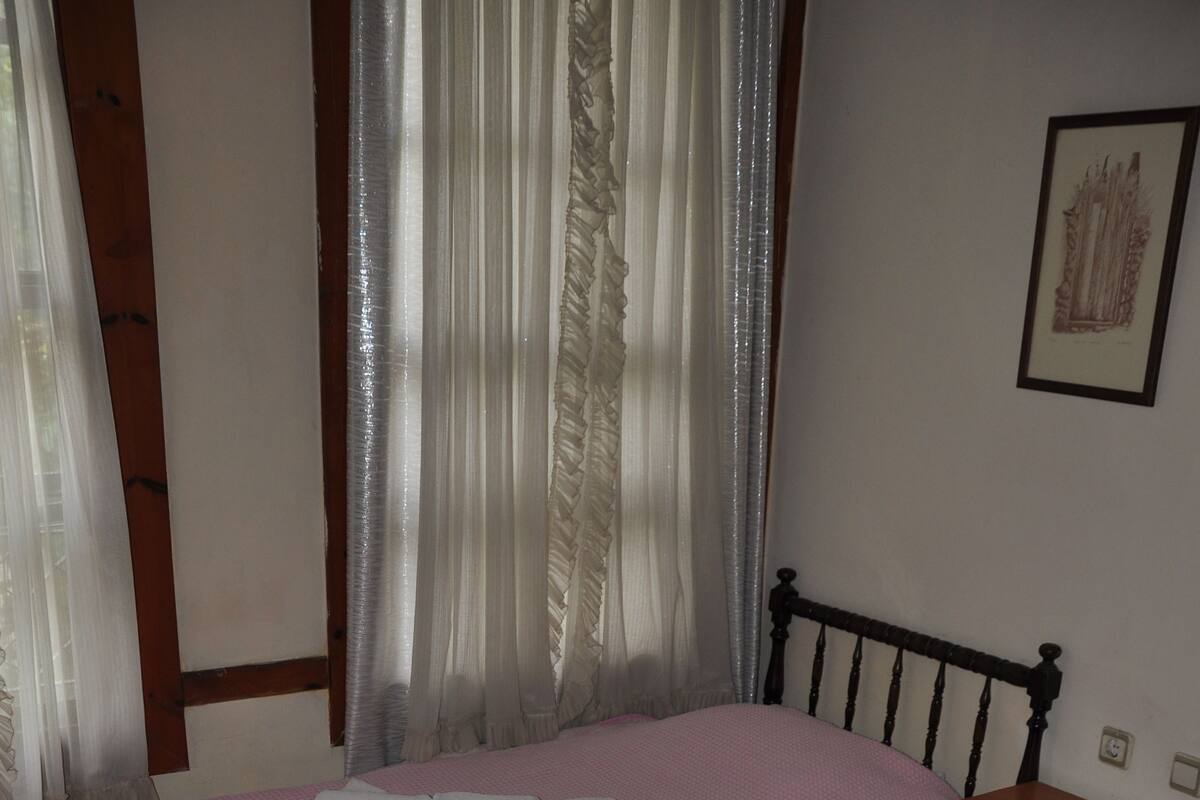 Une chambre avec deux lits, une table de chevet en bois, un tableau accroché au mur et une fenêtre avec des rideaux.