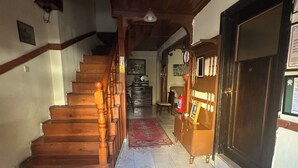 A wooden staircase leading to a second floor, a tiled floor with a patterned rug, a wooden cabinet, and a door with a sign. - Kont Pansiyon (Antalya)
