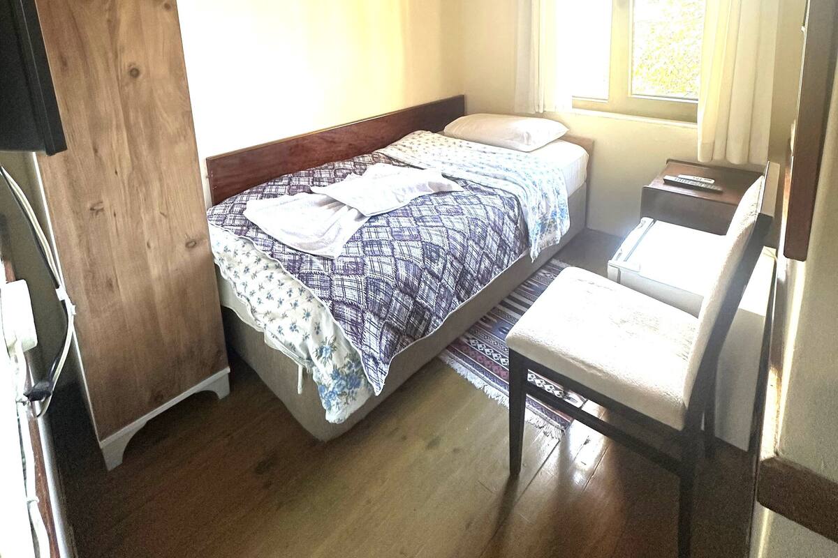 Une pièce comprenant un lit, un bureau, une chaise, une fenêtre avec des rideaux et un plafond en bois.