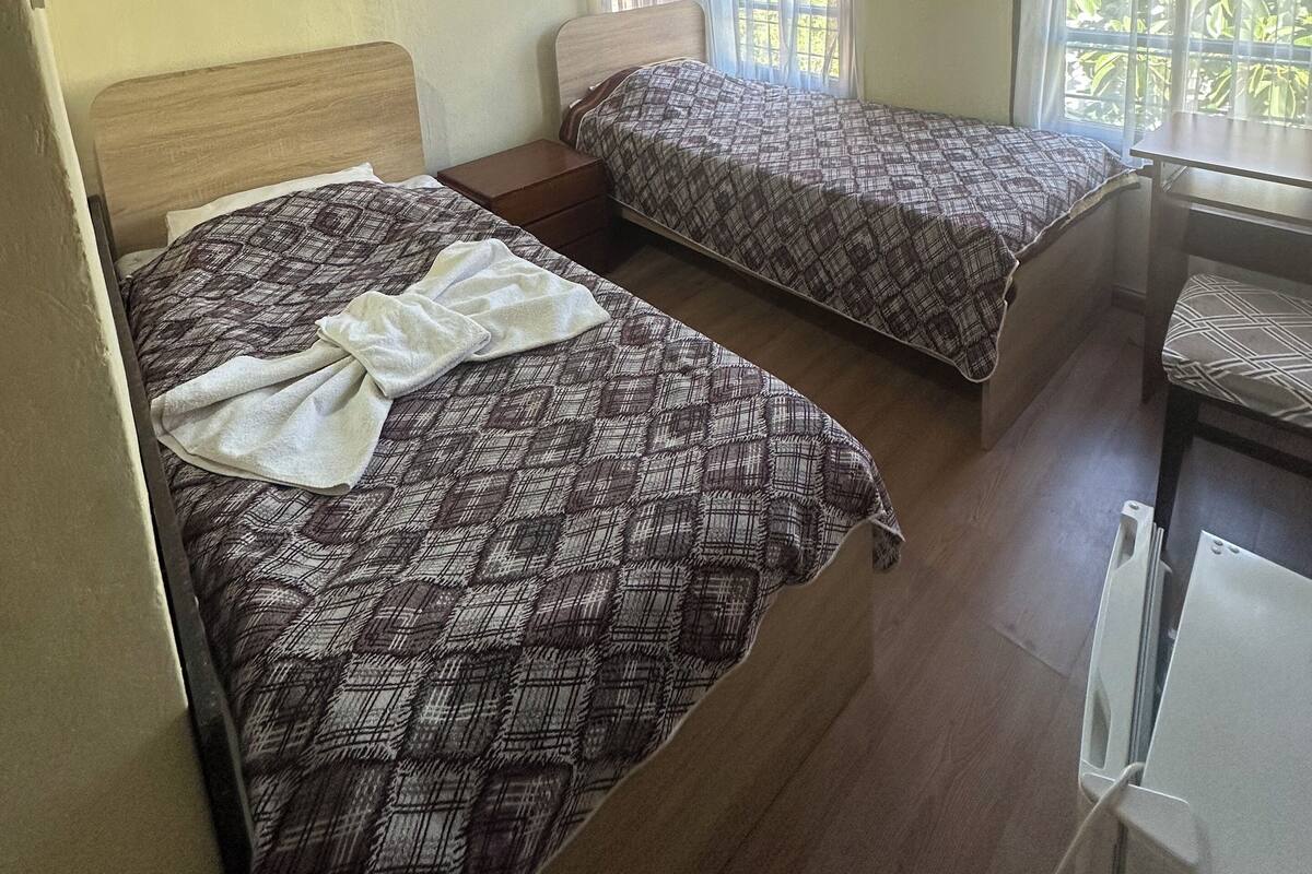 Une chambre avec deux lits, un plafond en bois, un appareil de climatisation et une fenêtre avec des rideaux.