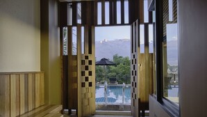 Blick auf einen Poolbereich mit Holzterrasse und Glastür, welche zu einem Pool mit Bergblick führt.