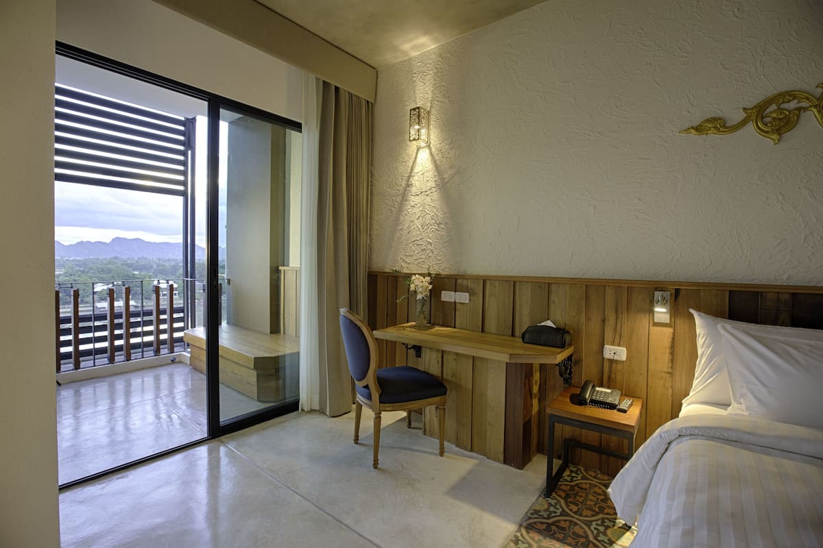 Habitació d'hotel amb balcó, escriptori, cadira, taulella de nit amb telèfon i llit.