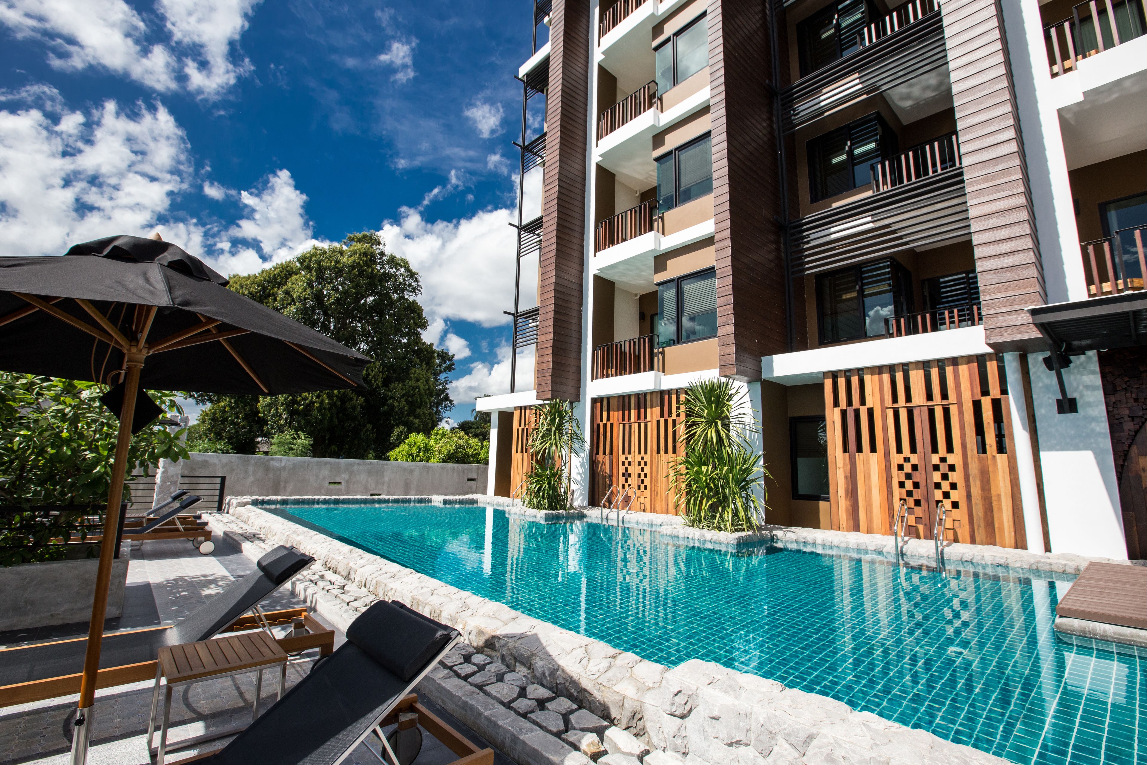 Ein Pool mit Liegestühlen und Sonnenschirmen, umgeben von einem modernen Gebäude mit Balkonen.