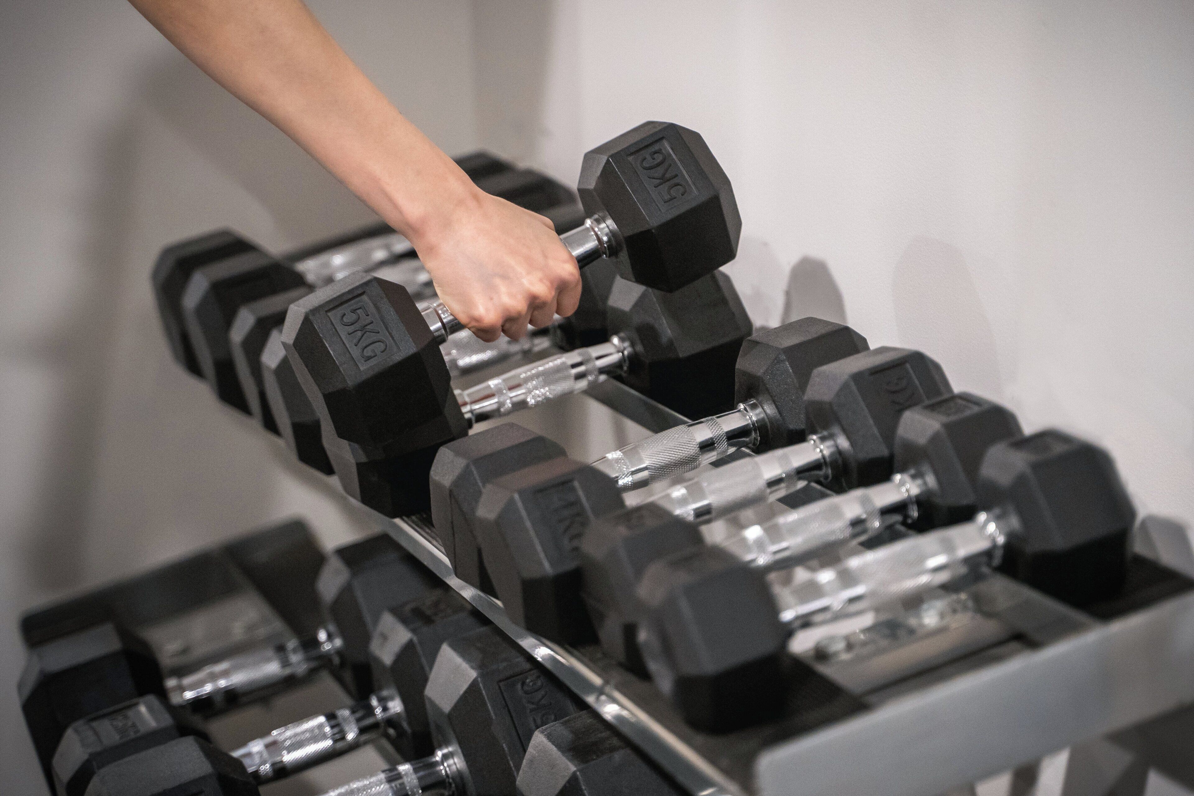 A hand lifting a 5kg dumbbell from a rack of similar weights.