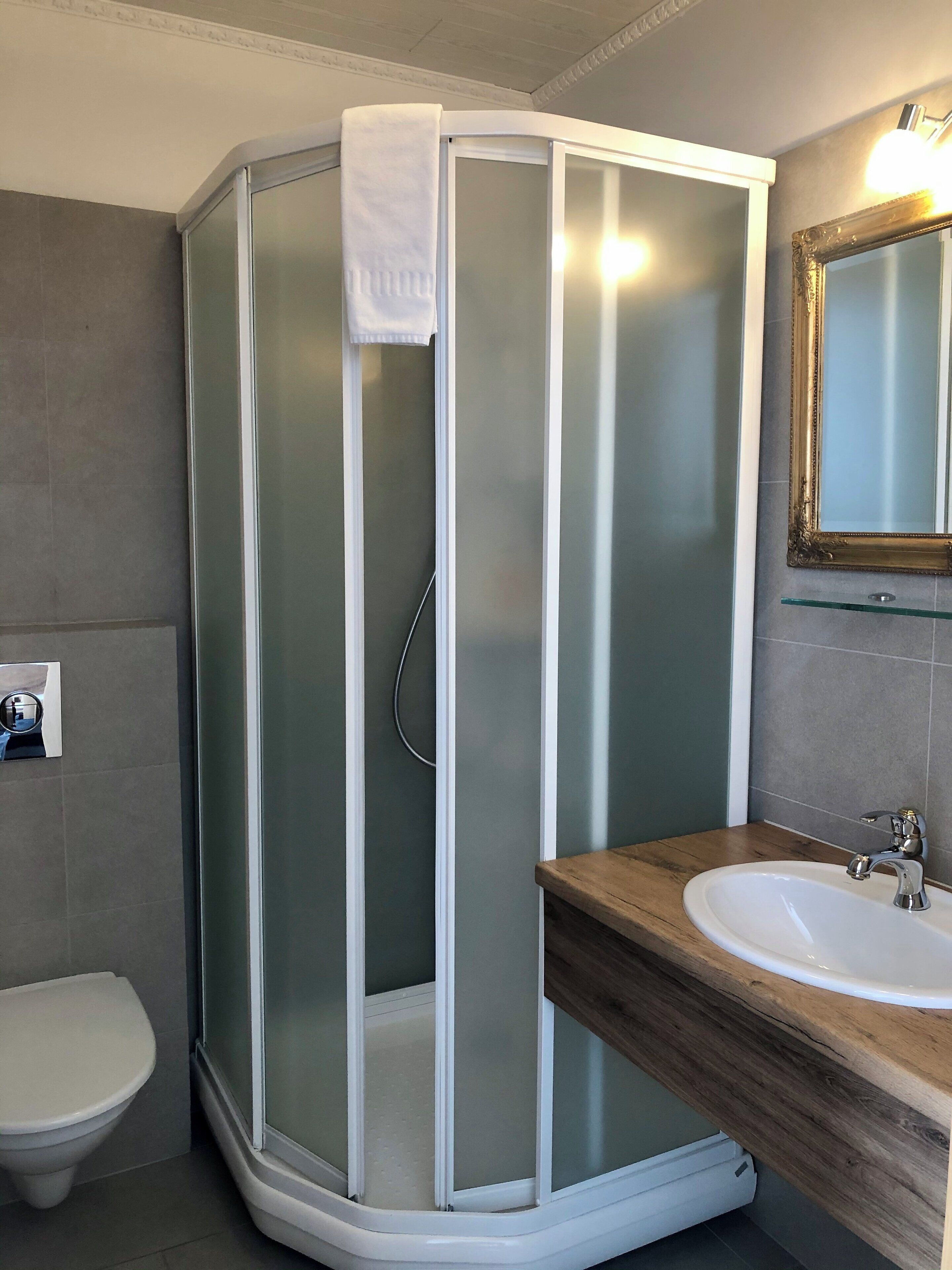 Un baño con ducha acristalada, tocador de madera con lavamanos y un espejo sobre el tocador.