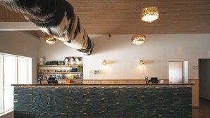 A reception area with a stone counter, wooden shelves with various items, and three pendant lights. - Hótel Dyrhólaey (Vik I Myrdal)