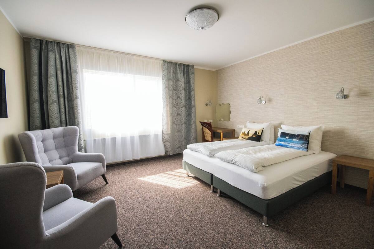 A hotel room with a bed, two armchairs, a small table, and a nightstand.