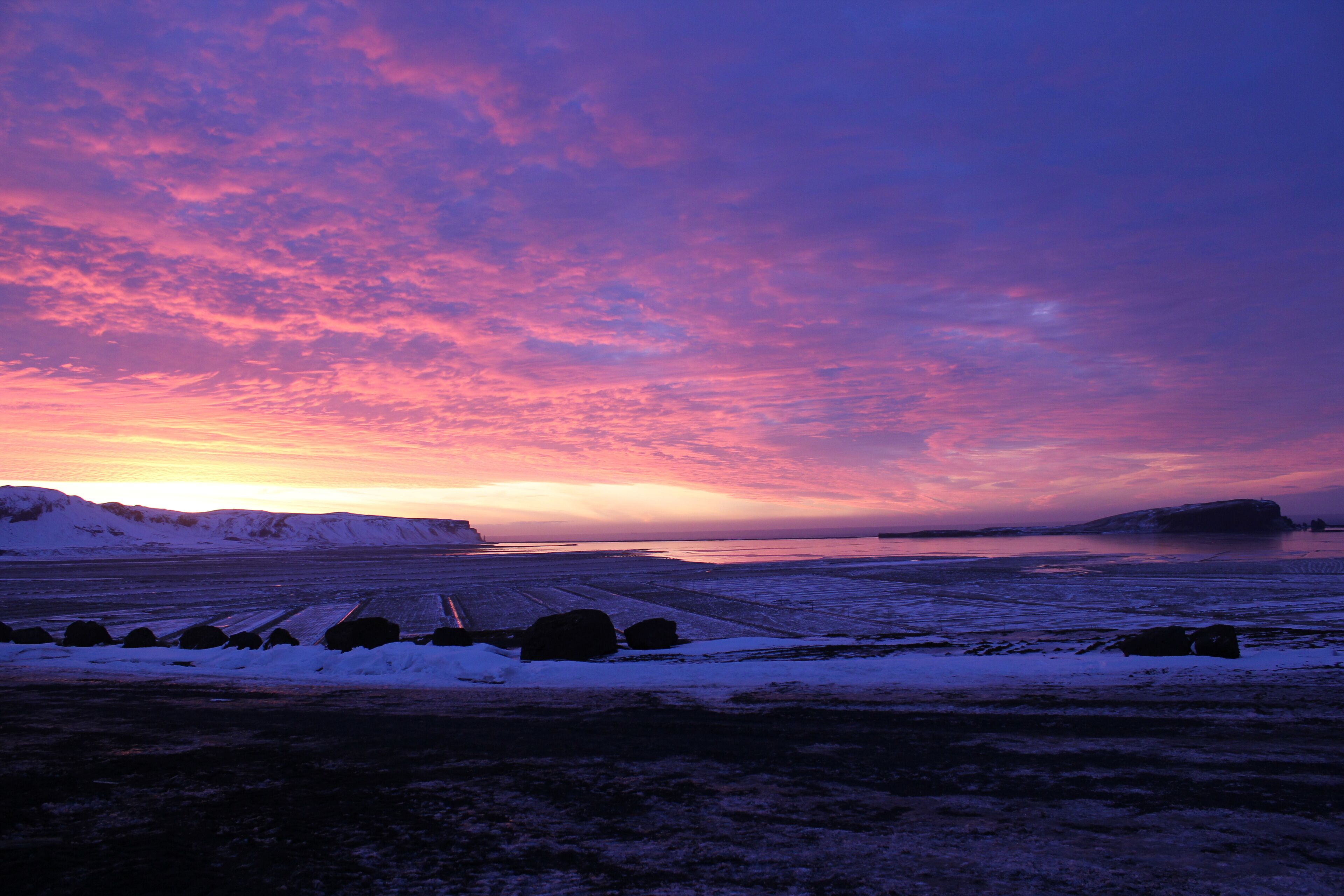 A snowy landscape with a sunset and a body of water in the distance.