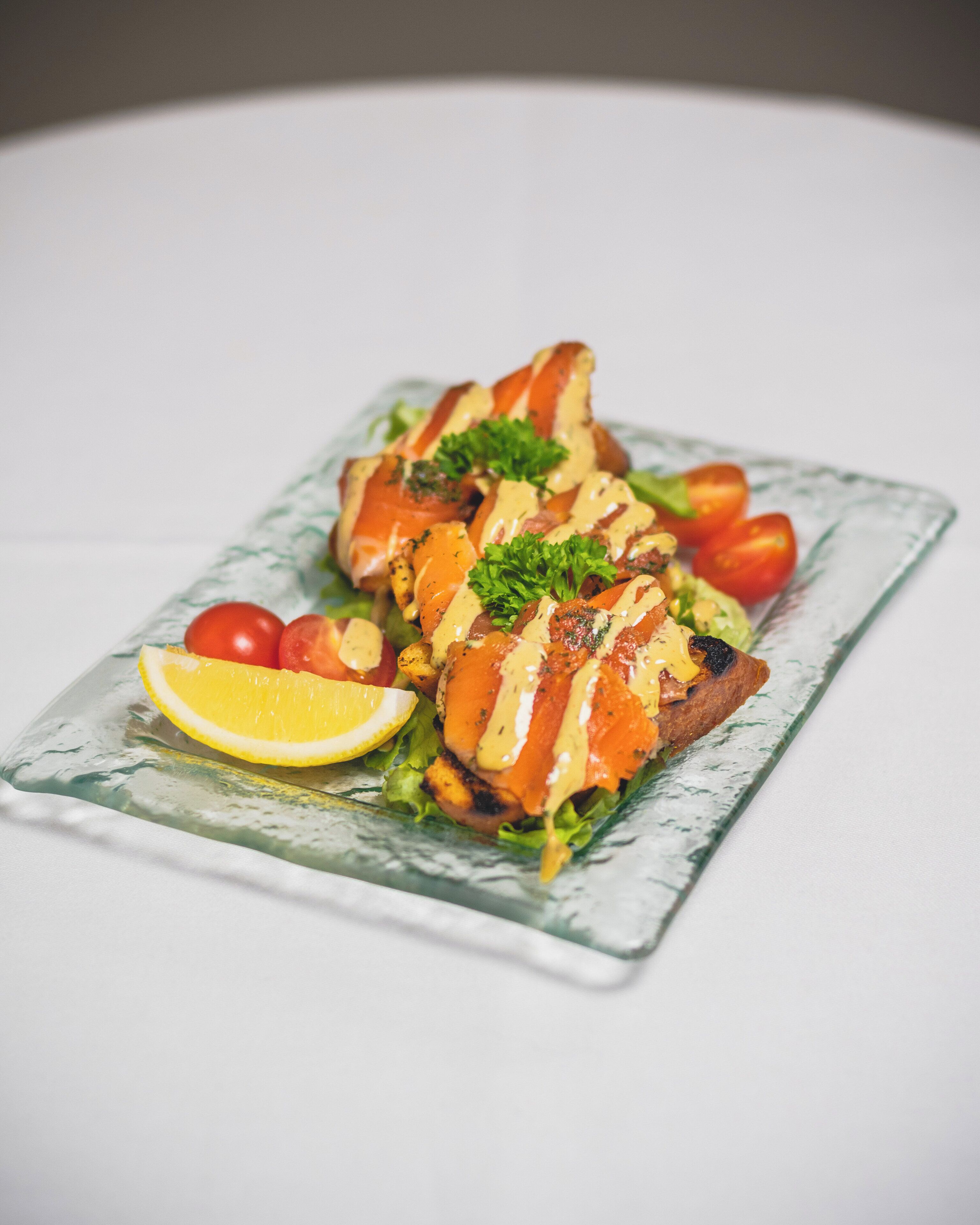 Un plato de comida con salmón, tomates y un gajo de limón.