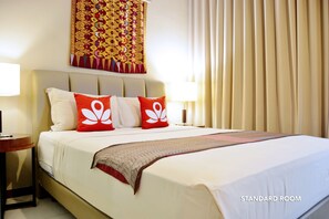 A standard room with a bed, a nightstand, a lamp, a tapestry, and curtains.