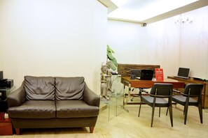 A modern living room with a leather sofa, a glass coffee table, and a wooden desk with a laptop and a sign. - W Home Cipete (Jakarta)